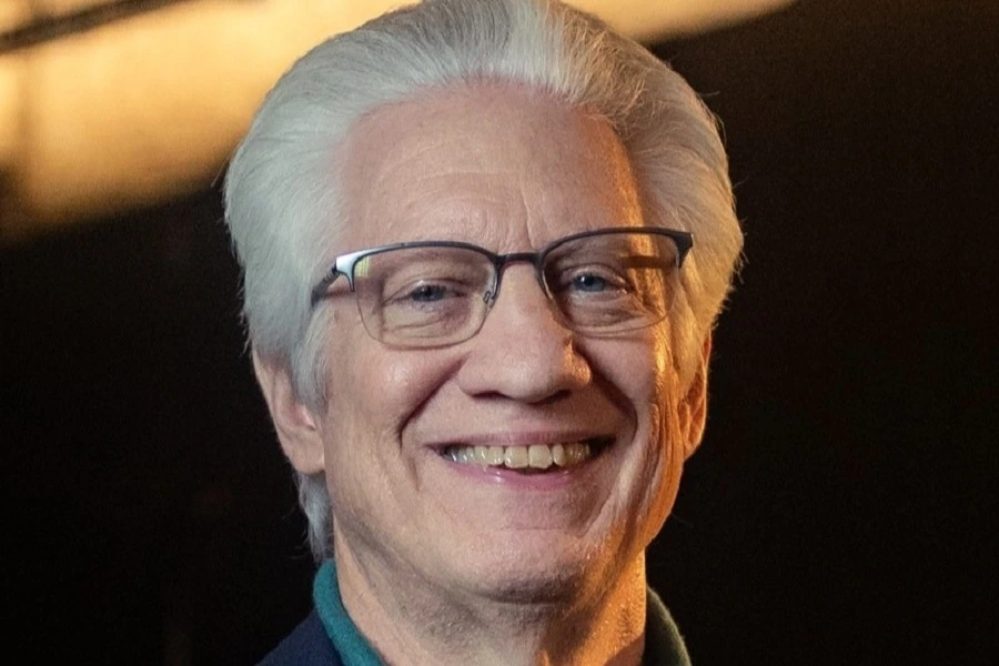 mature man with grey hair smiling against black background